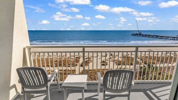A balcony with a view of the beach and ocean, featuring two chairs and a small table. - Oceanfront Oasis: Your Ideal 1BR Condo Escape (Myrtle Beach)