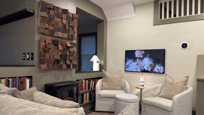 A modern living room with a fireplace, a mounted TV, and a bookshelf. - THE MILL HOUSE - Charming Historic Cottage 1.5 miles from the US Open (Oakmont)