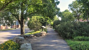A paved pathway lined with trees and shrubs, leading to a building with a sign. - THE MILL HOUSE - Charming Historic Cottage 1.5 miles from the US Open (Oakmont)