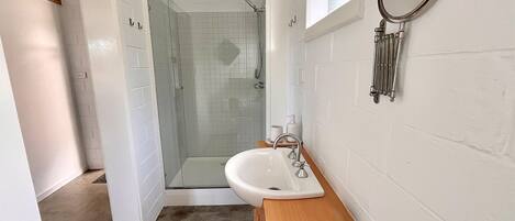 A bathroom with a glass-enclosed shower, a white sink, and a wooden cabinet.