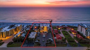 Luftaufnahme eines Küstenhotels mit Parkplatz, Gebäuden und Blick auf den Ozean bei Sonnenuntergang.