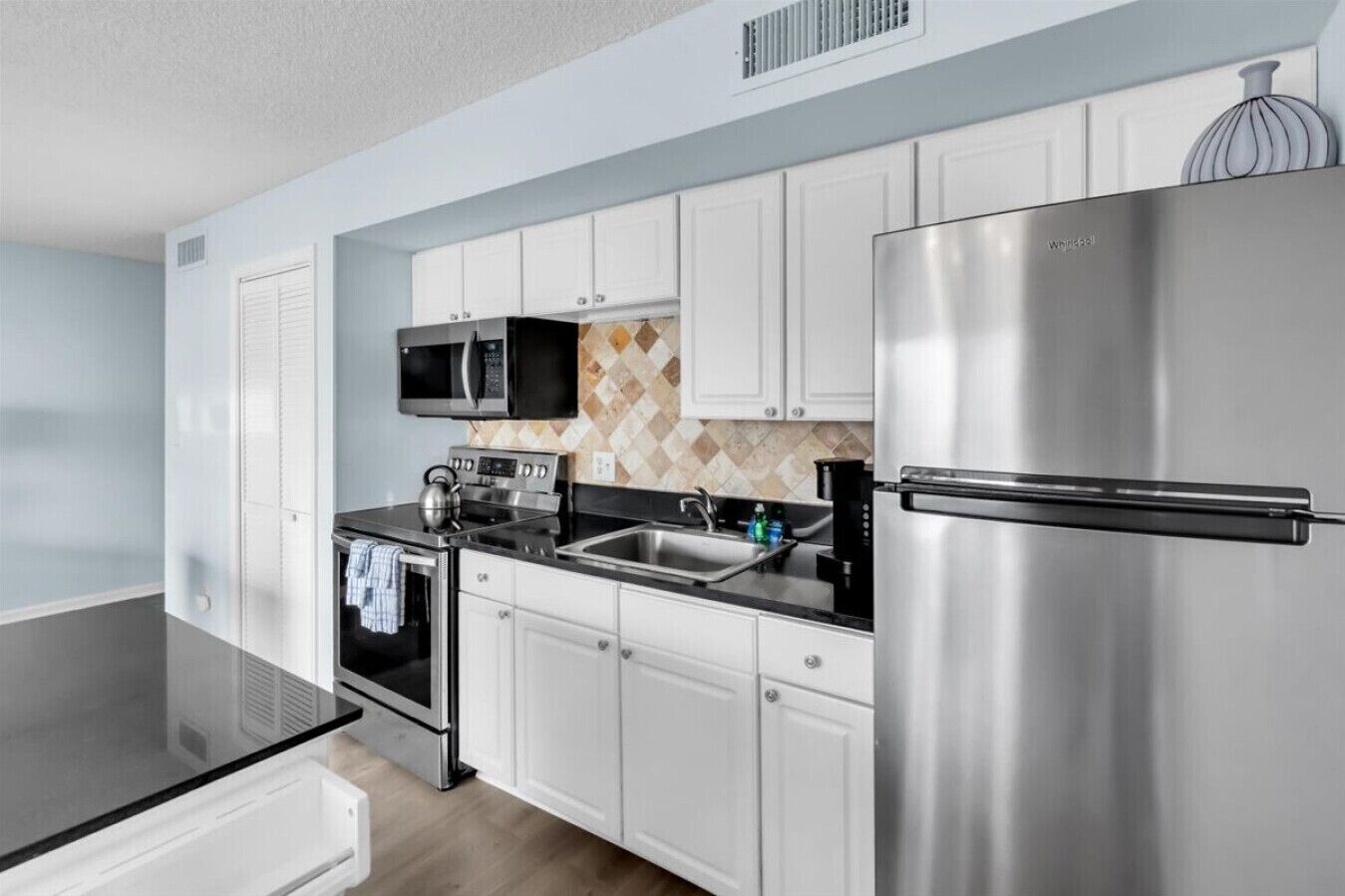 A modern kitchen with stainless steel appliances, white cabinetry, and a microwave above the stove.