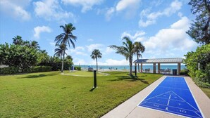 Ein gepflegter Rasen mit einem Shuffleboard-Spielfeld, Palmen und einem Pavillon mit Blick auf einen Strand.