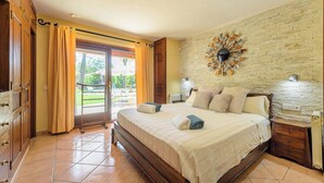 A bedroom with a large bed, a wooden wardrobe, a brick wall, and a view of the outdoors through a sliding door. - New! Villa Beni - Santa Eulalia (Ibiza)