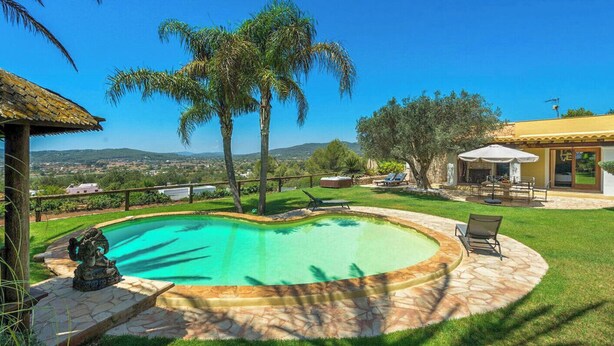 A swimming pool with a stone border, surrounded by a well-maintained lawn and palm trees. - New! Villa Beni - Santa Eulalia (Ibiza)