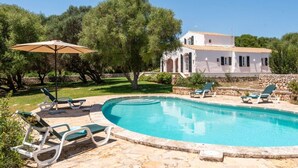 A pool area with lounge chairs and an umbrella, surrounded by greenery and a white building with arches. - New! Casa Nova de Biniparrell (Biniparrell)
