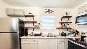 Cocina moderna con armarios blancos, refrigerador de acero inoxidable, letrero de café y diversos electrodomésticos.