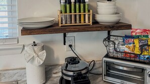 Una cocina con un estante de madera que contiene cristalería, una cafetera y un tostador.
