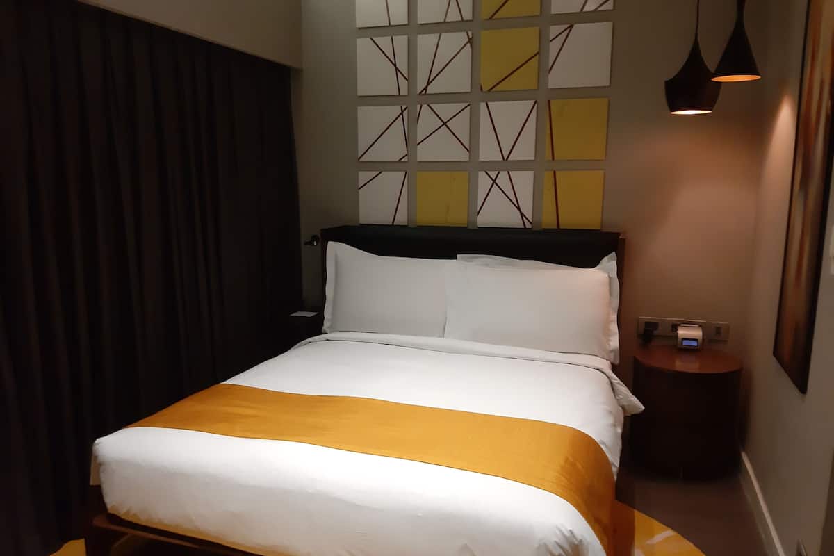 A hotel room with a bed, a nightstand, a wall with geometric patterns, and a lamp.