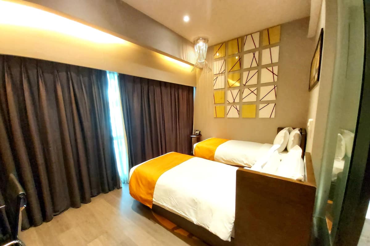 A hotel room with two beds, a desk, a chair, and a large window with curtains.