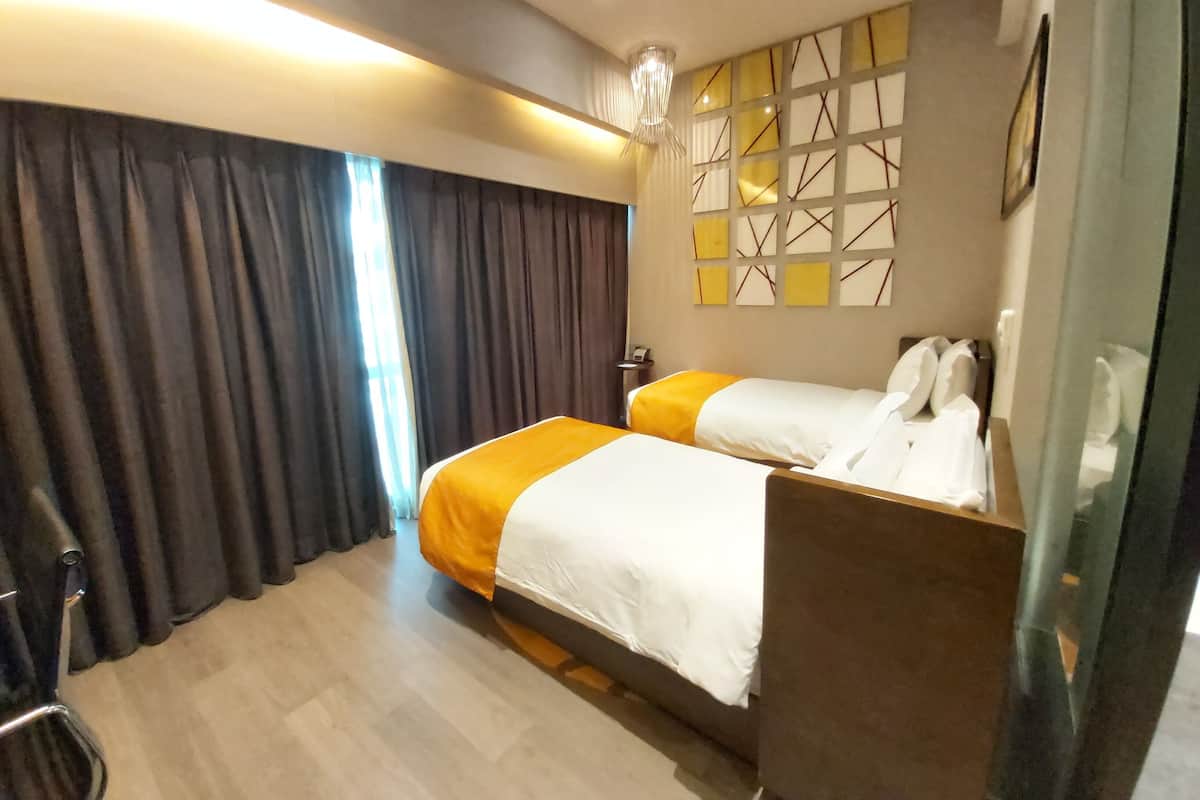 A hotel room with two beds, a desk, a chair, a large window with curtains, and a wall with a geometric pattern.