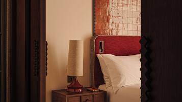 Un dormitorio con una mesita de noche de madera, una lámpara, una cama con cabecera roja y una alfombra estampada.