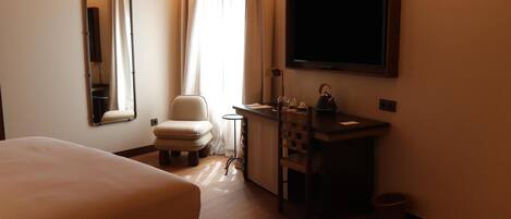 Habitación de hotel con cama, una silla, escritorio con lavamanos, espejo y televisión.