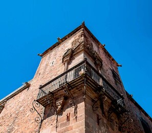 Ein historisches Gebäude mit einem markanten Eckturm, aufwendigen Eisengeländern und blauem Himmel im Hintergrund.