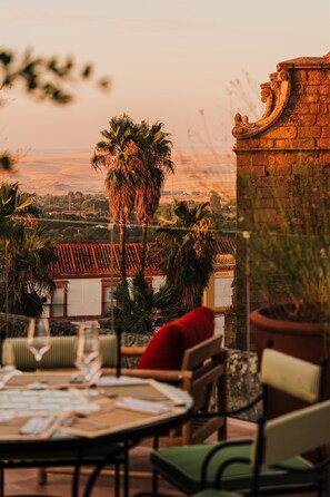 A dining area with a table set for two, overlooking a scenic view with palm trees and a distant landscape. - Palacio De Godoy Caceres, Curio Collection By Hilton (Cáceres)