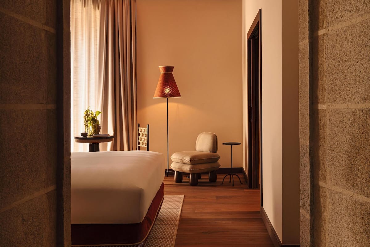 A narrow hallway leading to a bedroom with a bed, a lamp, and a small table.