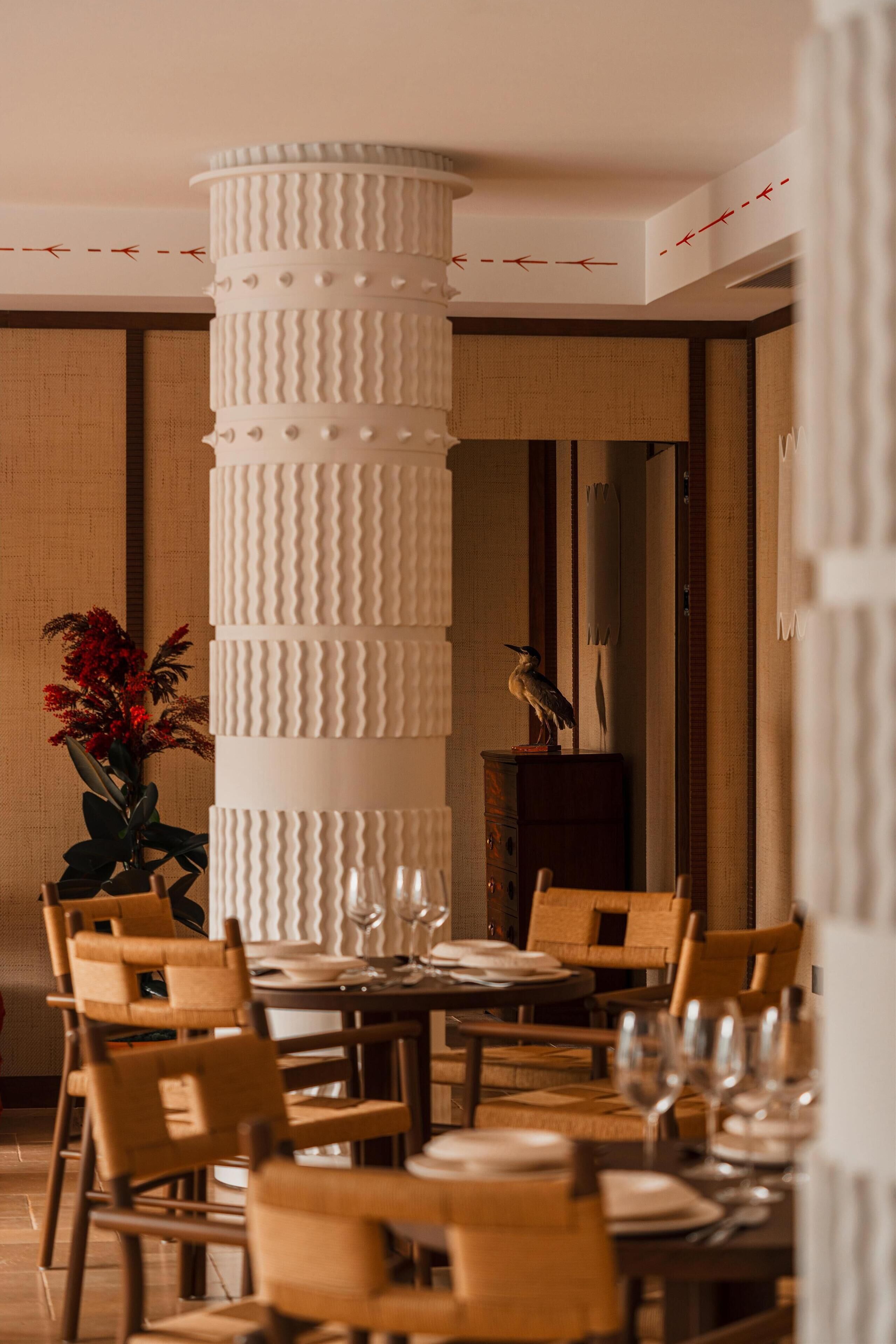 A dining area with a tall, textured column, wooden chairs, and a table set for a meal.