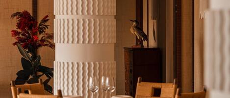 A dining area with a tall, textured column, wooden chairs, and a table set for a meal.