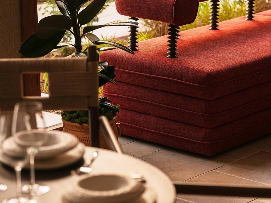 A dining area with a table set for two, a red upholstered chair, and a potted plant.