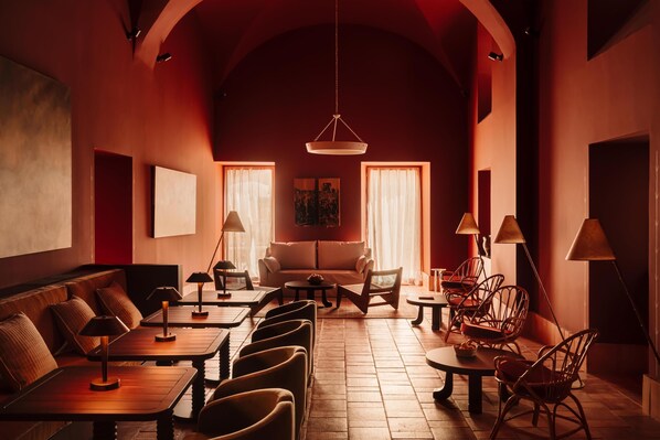 A cozy, well-lit lounge area with a sofa, tables, and chairs, featuring a warm color scheme and a high ceiling. - Palacio De Godoy Caceres, Curio Collection By Hilton (Cáceres)