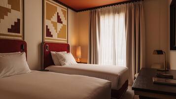 Habitación de hotel con dos camas, un escritorio, una lámpara y una ventana con cortinas.