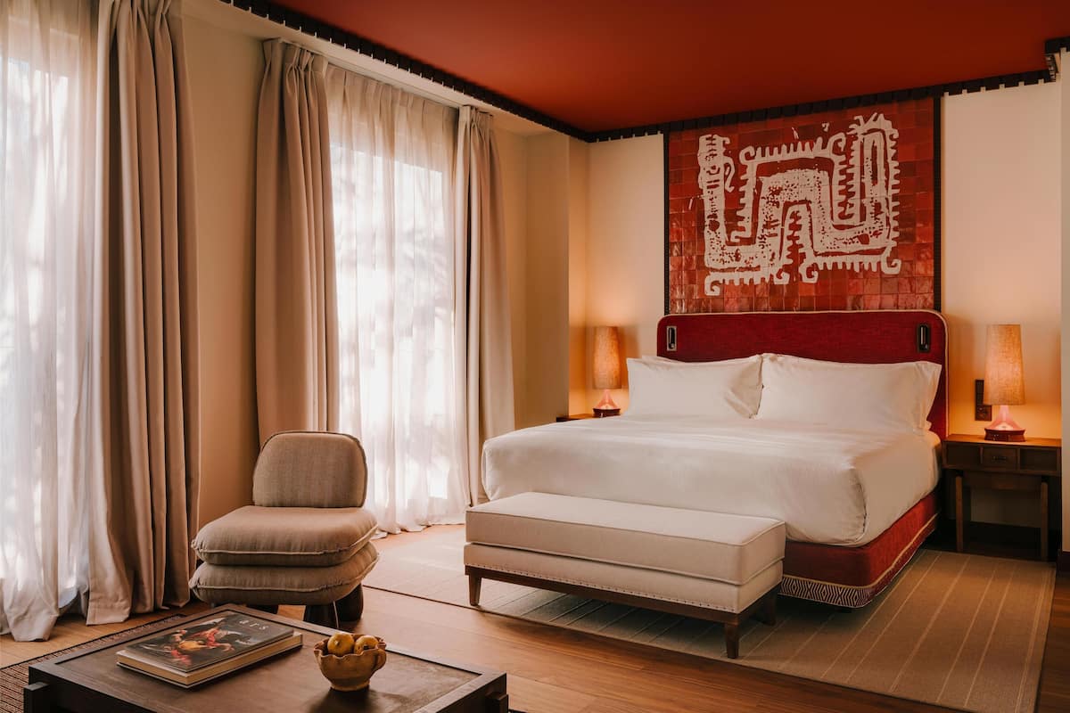 A hotel room with a large bed, a chair, a bedside table, and a wall with a decorative pattern.