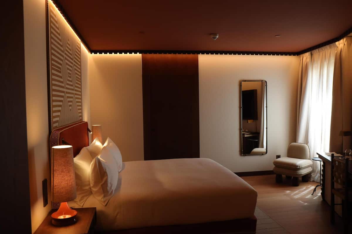 A hotel room with a bed, bedside lamp, chair, and a mirror.
