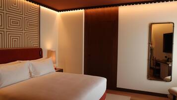 A neatly made bed with white linens, a wooden headboard, a wall-mounted mirror, and a door with a wooden panel.