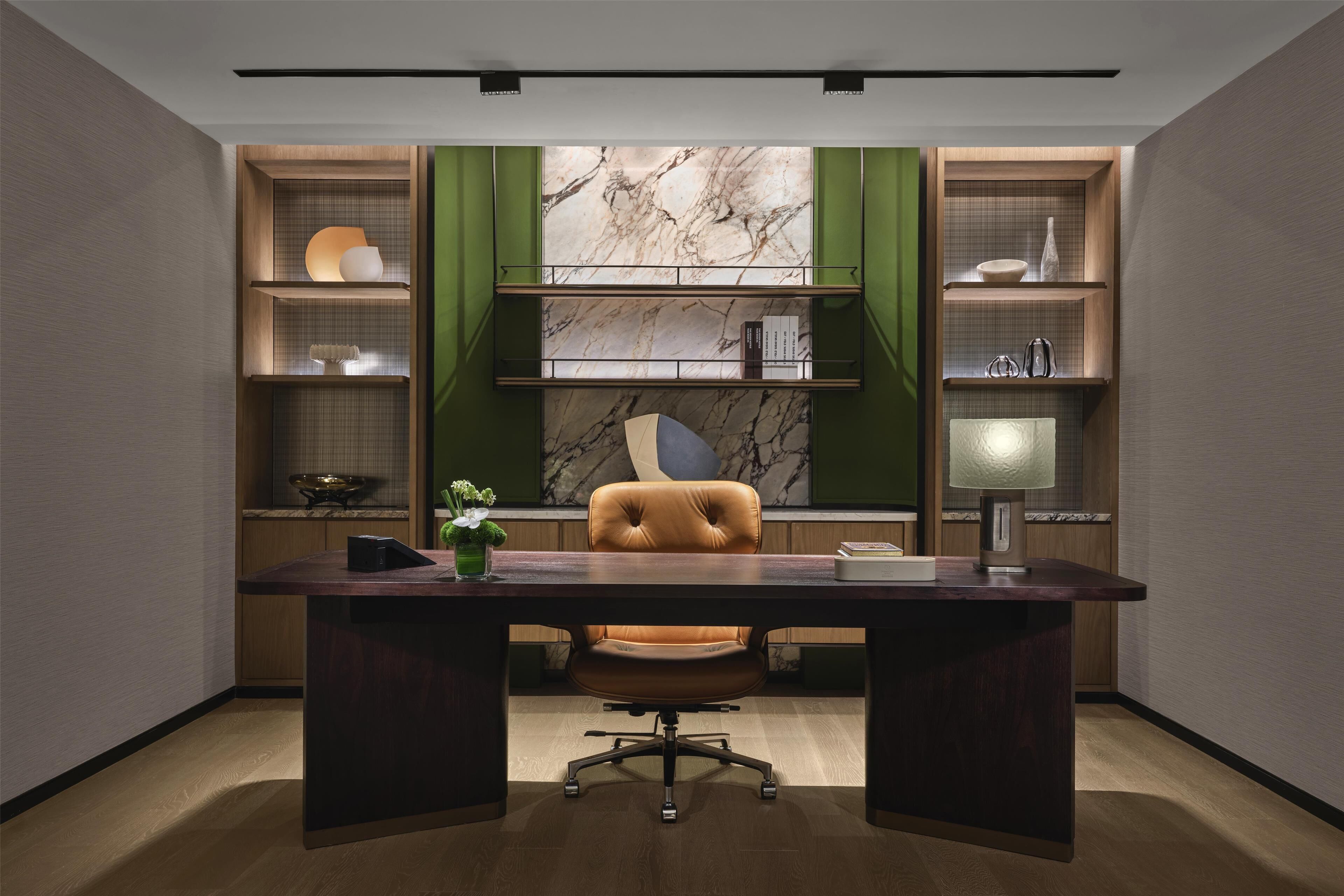 A modern office with a dark wood desk, a leather chair, and green shelving units with marble backdrops.