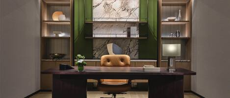 A modern office with a dark wood desk, a leather chair, and green shelving units with marble backdrops.