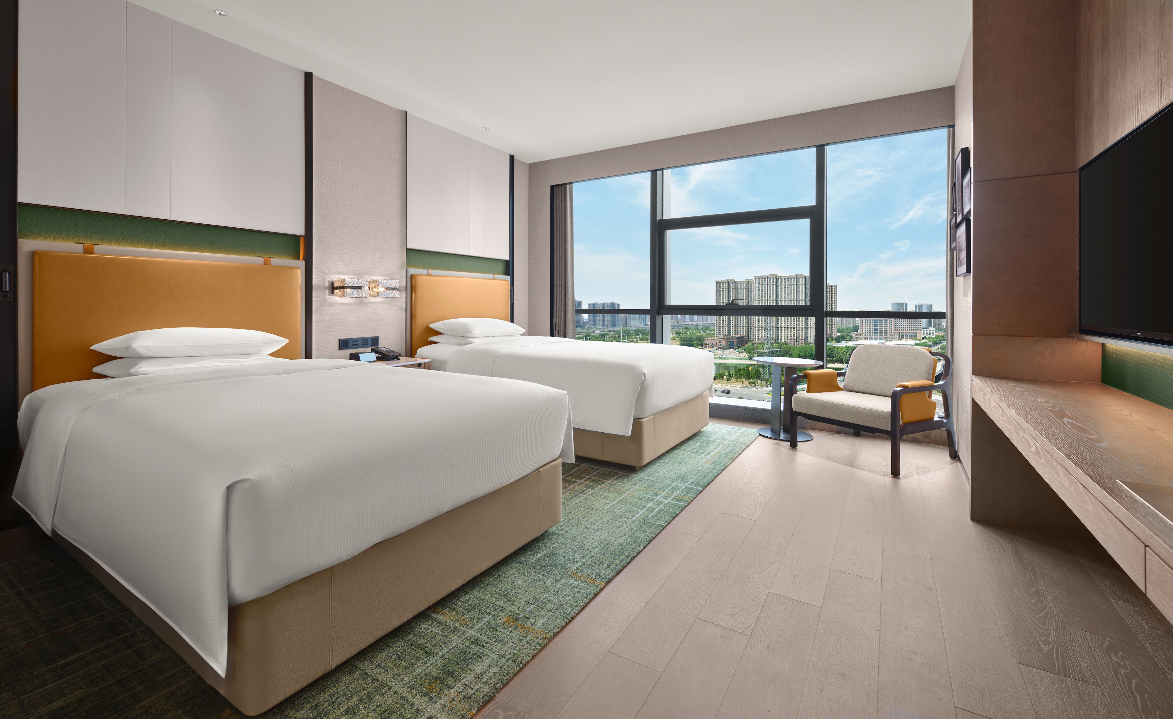 A hotel room with two beds, a seating area, a TV, and a view of the cityscape.