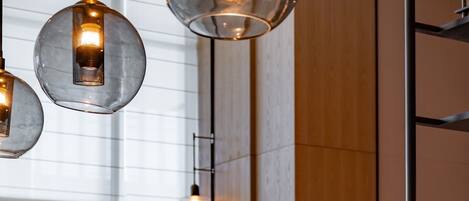 Interior moderno com um balcão comprido exibindo diversas tigelas e utensílios, luminárias pendentes e uma grande janela que permite a entrada de luz natural.