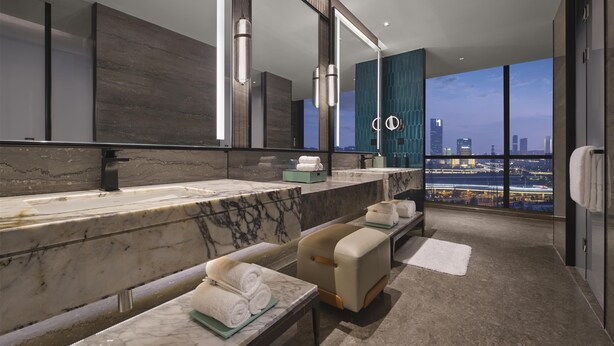 Un baño moderno con un espejo grande, encimeras de mármol y un banco con toallas.