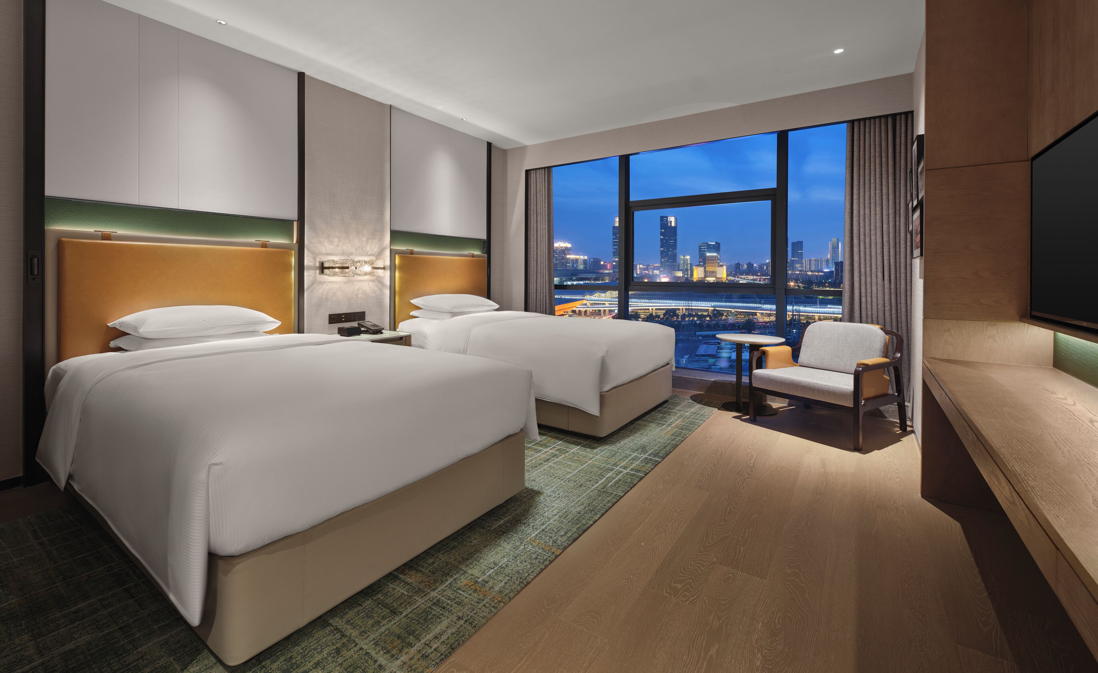 A hotel room with two beds, a seating area, a TV, and a city view.