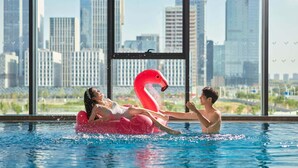 Una piscina con vista a la ciudad, un flotador de flamenco rosa y una persona interactuando con él.
