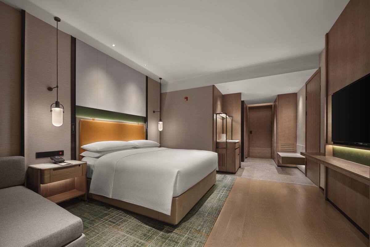 A modern hotel room with a large bed, bedside tables, a TV, and a walk-in closet.