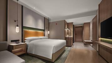A modern hotel room with a large bed, bedside tables, a TV, and a walk-in closet.