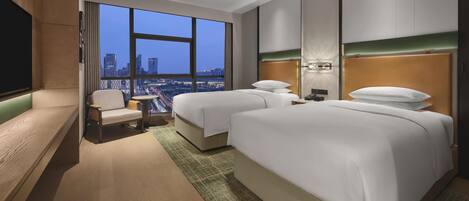 A hotel room with two beds, a TV, a chair, and a large window with a city view.