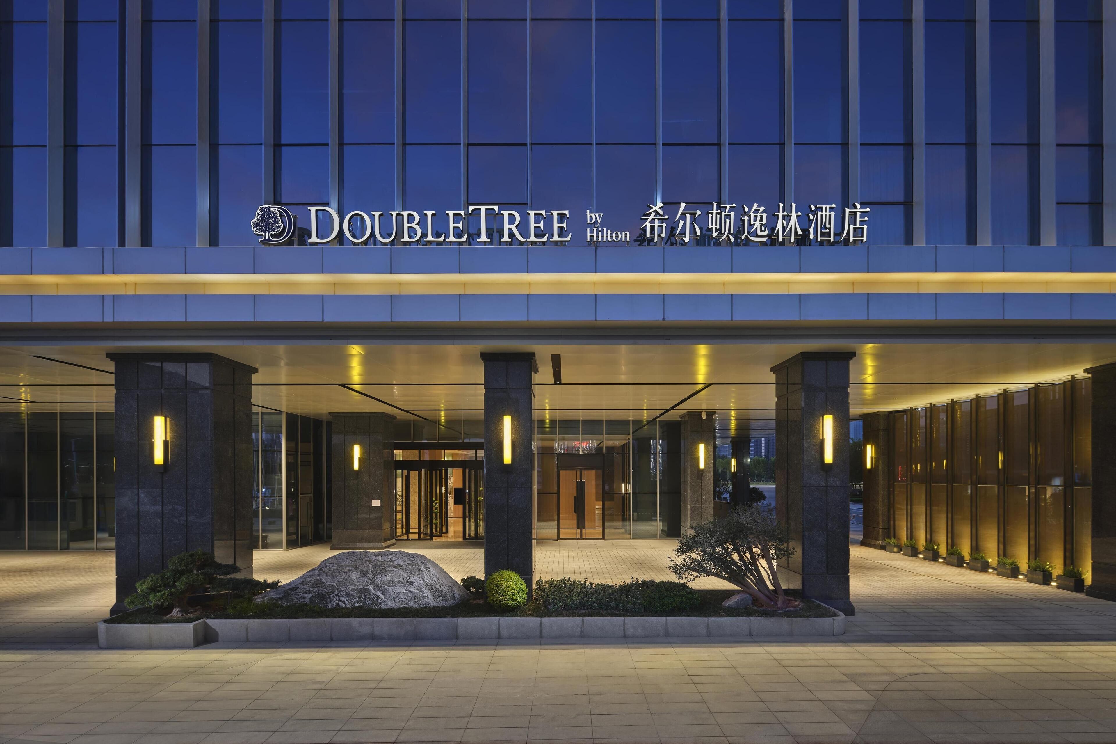 The exterior of the DoubleTree by Hilton hotel with a modern facade, large glass windows, and illuminated signage.