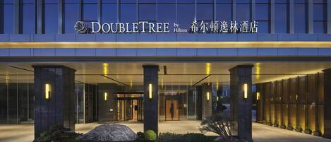 The exterior of the DoubleTree by Hilton hotel with a modern facade, large glass windows, and illuminated signage.