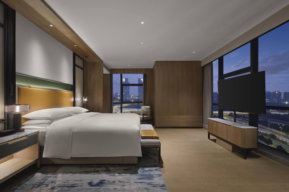 A modern hotel room with a large bed, a TV, and a city view.