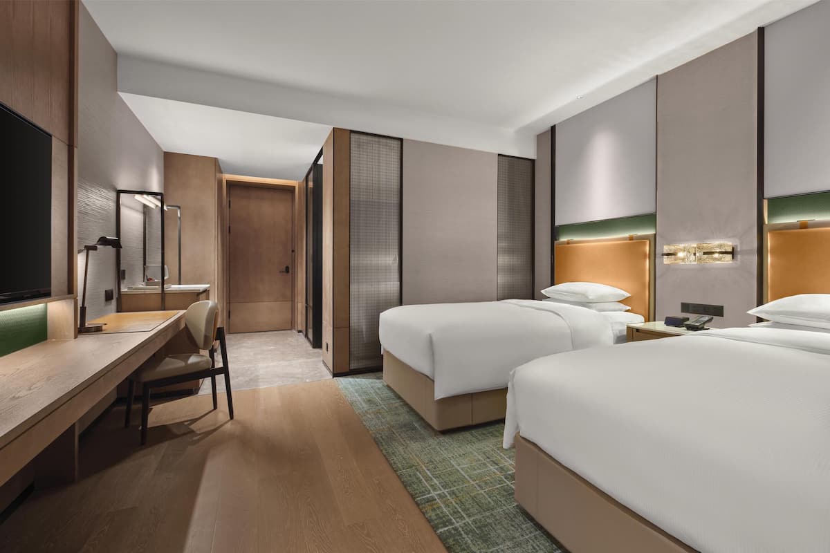 A modern hotel room with two beds, a desk, and a TV.