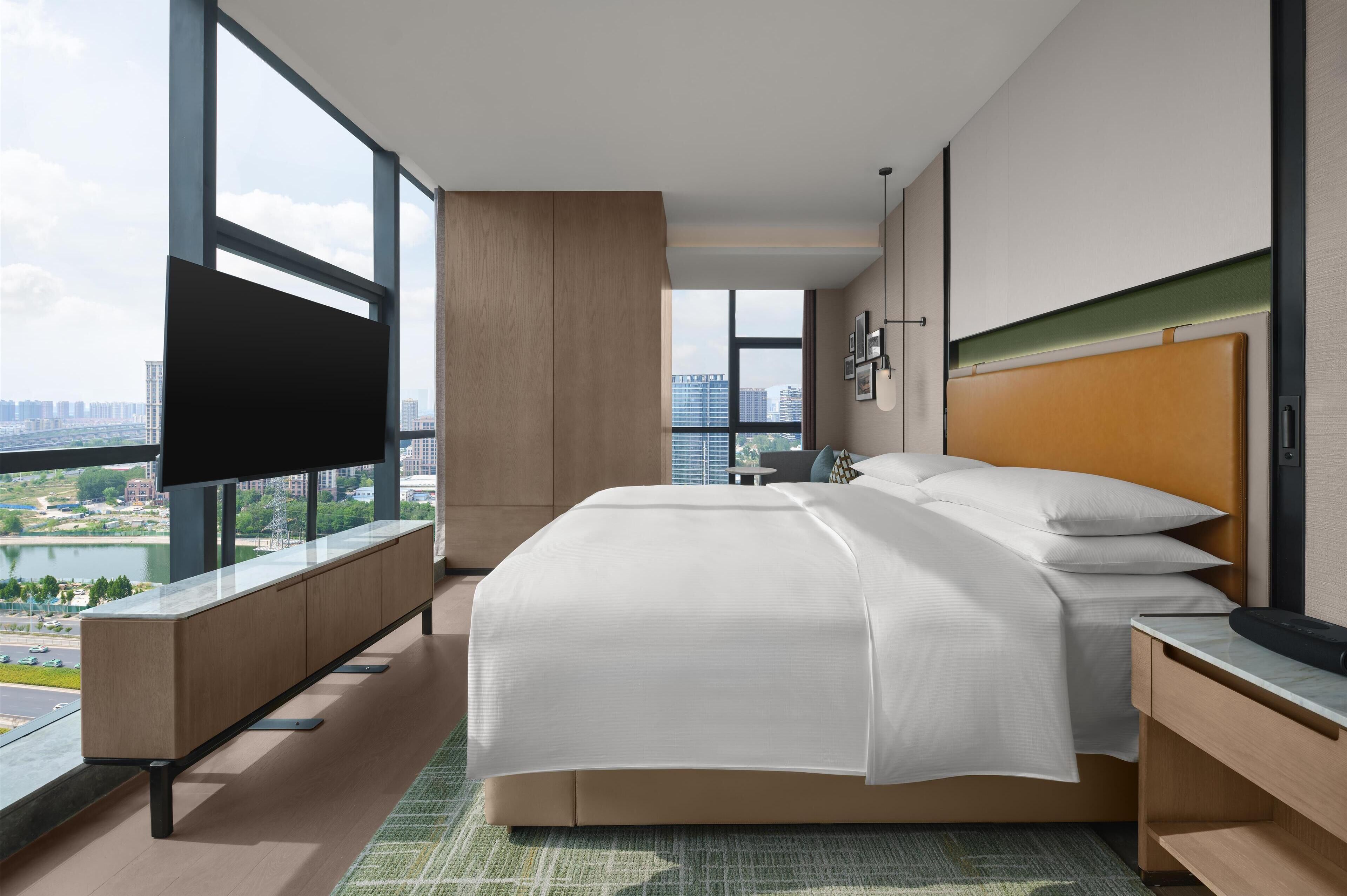 Habitación de hotel moderna con una cama grande, televisión de pantalla plana, vista a la ciudad y un balcón.