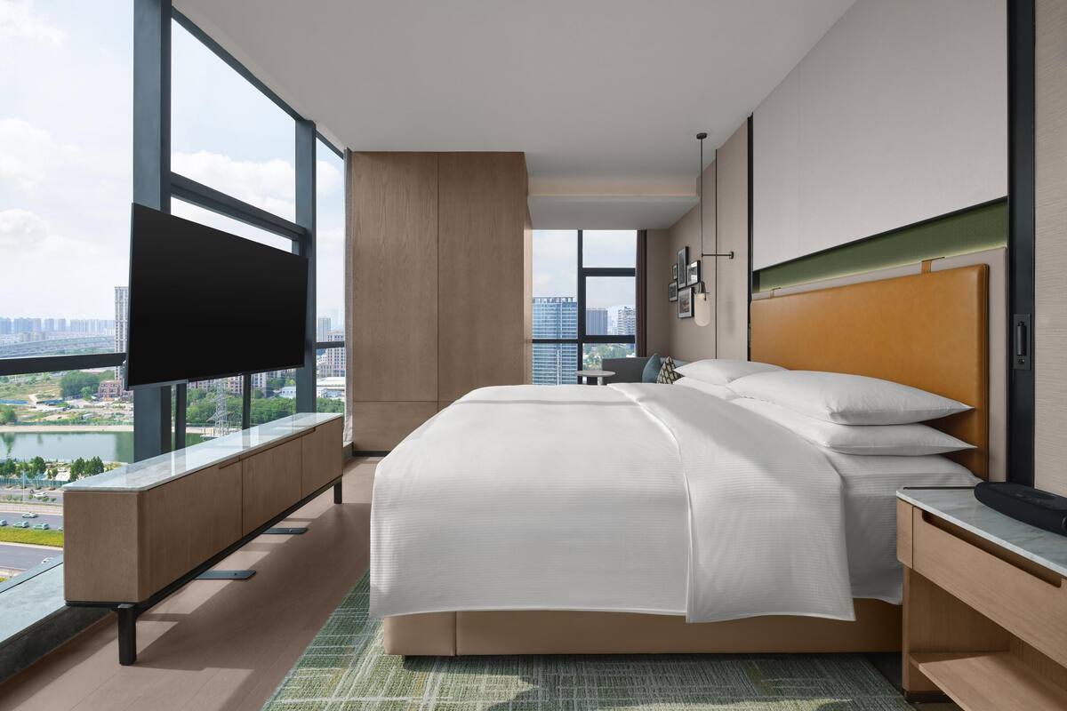 Habitación de hotel moderna con una cama grande, televisión de pantalla plana, vista a la ciudad y un balcón.