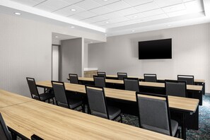 Un salón de conferencias con varias mesas y sillas, un televisor de pantalla plana montado en la pared y una puerta que da a otra sala.