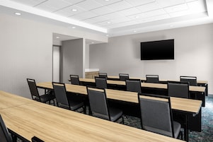 Un salón de conferencias con varias mesas y sillas, un televisor de pantalla plana montado en la pared y una puerta que da a otra sala.