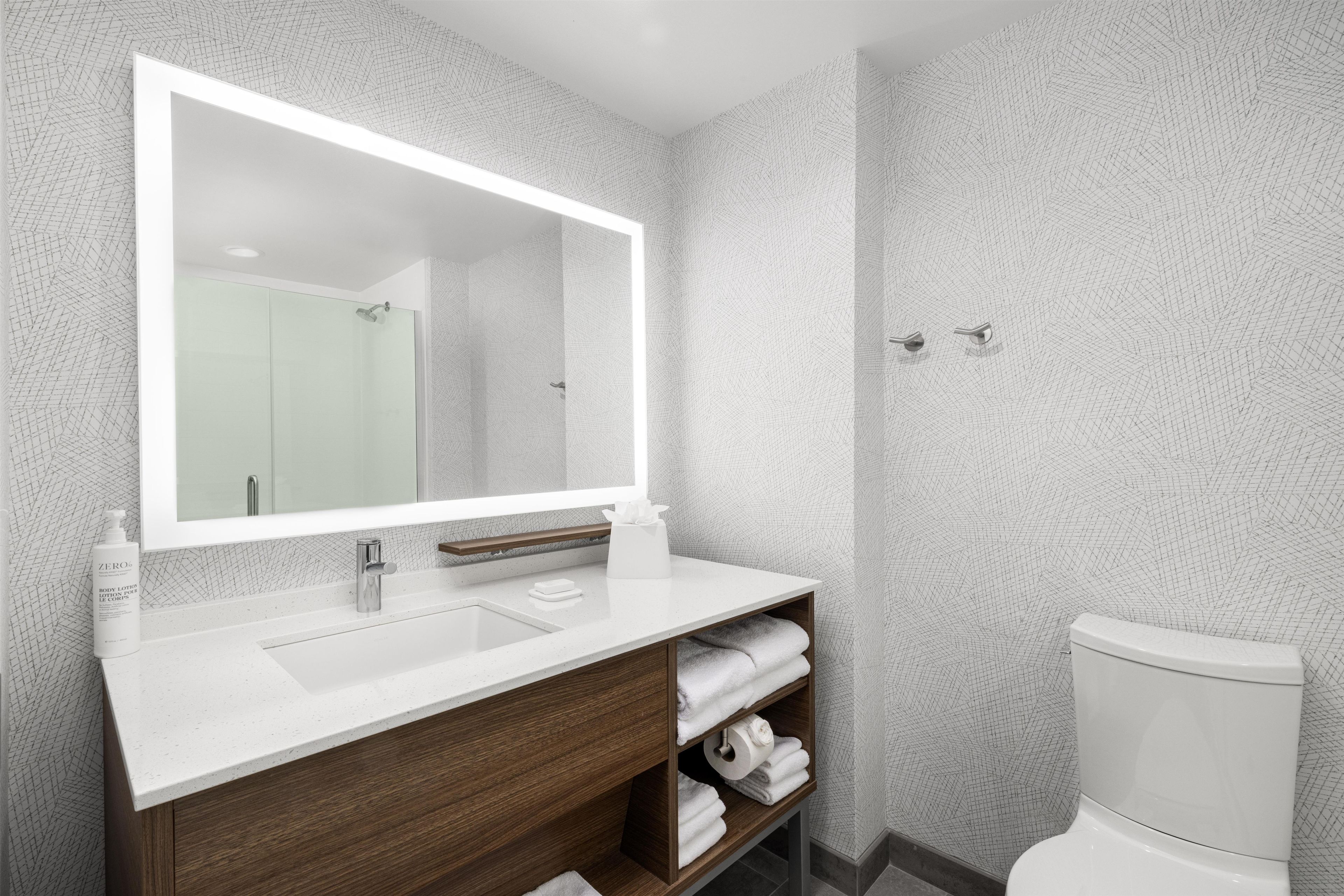 Un baño con un espejo grande, un lavabo, un inodoro y un toallero.
