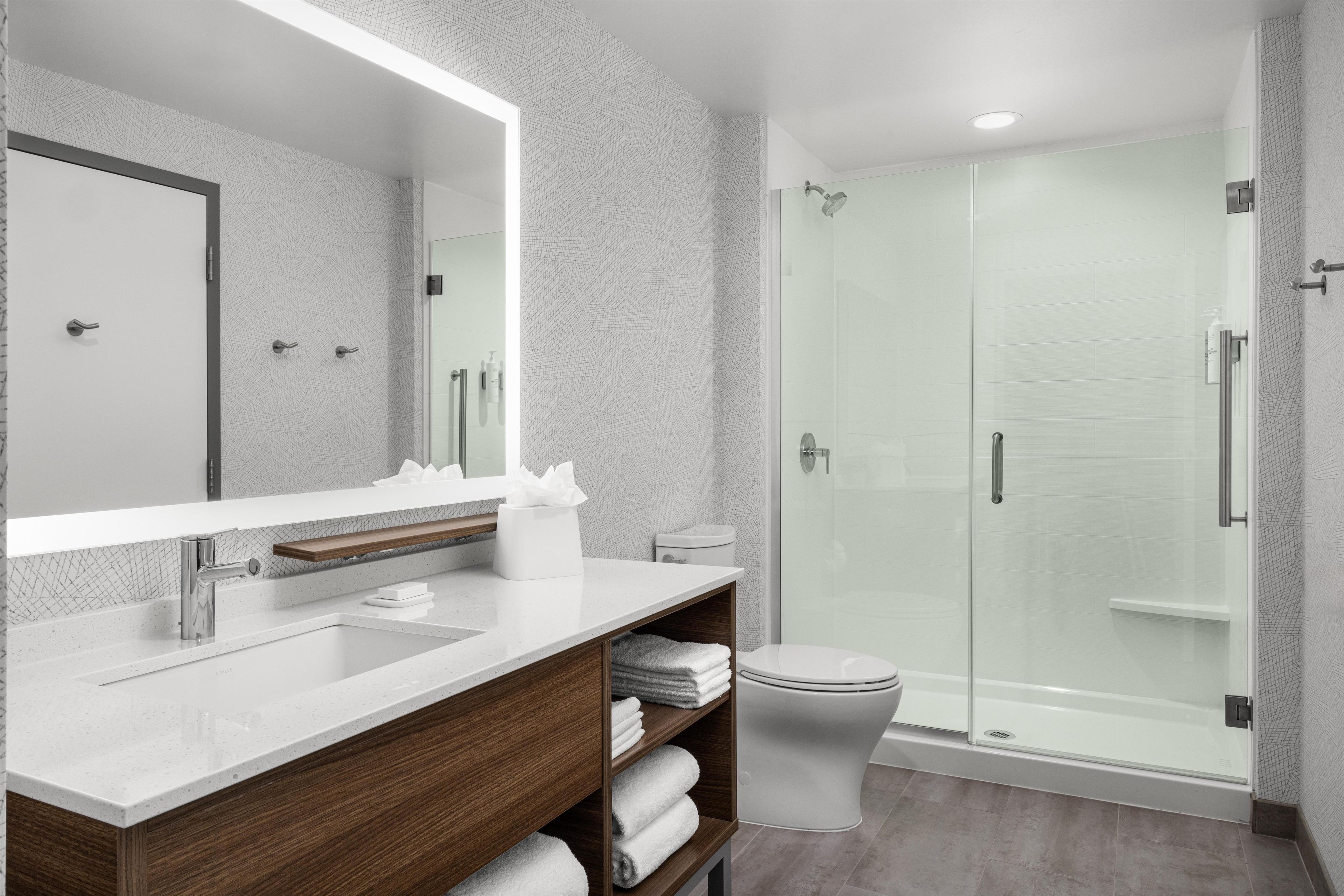 Une salle de bain moderne avec une douche à l’italienne en verre, un lavabo blanc avec un meuble-vasque en bois et un grand miroir.