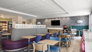 Ein modernes Restaurant mit einer Sitzgegend, die violette und türkisfarbene Sitzbänke, Holztische und blau gepolsterte Stühle bietet.