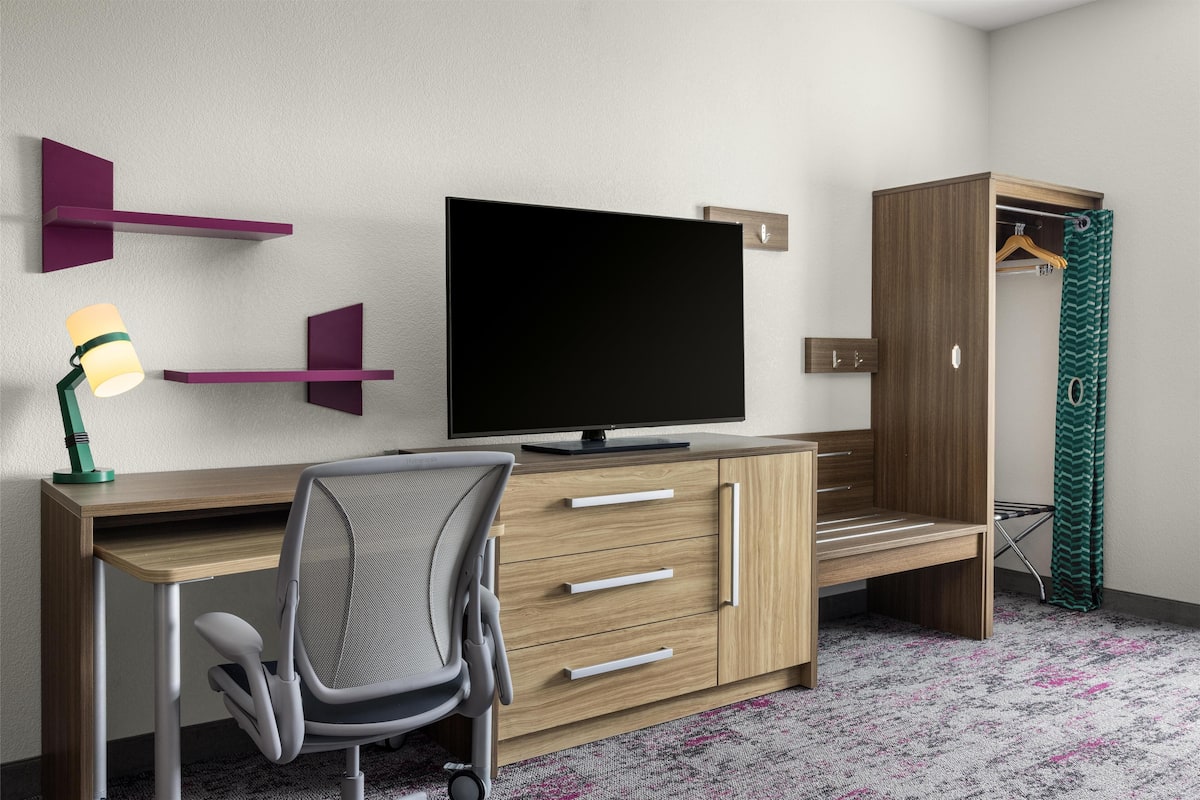 A modern bedroom with a wooden desk, a television, a chair, a wardrobe, and a hanging closet.